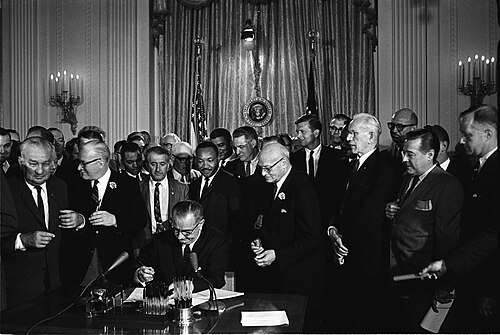 Pres. LBJ signs the 1964 Civil Rights Act as Martin Luther King, Jr., and others, look on.
